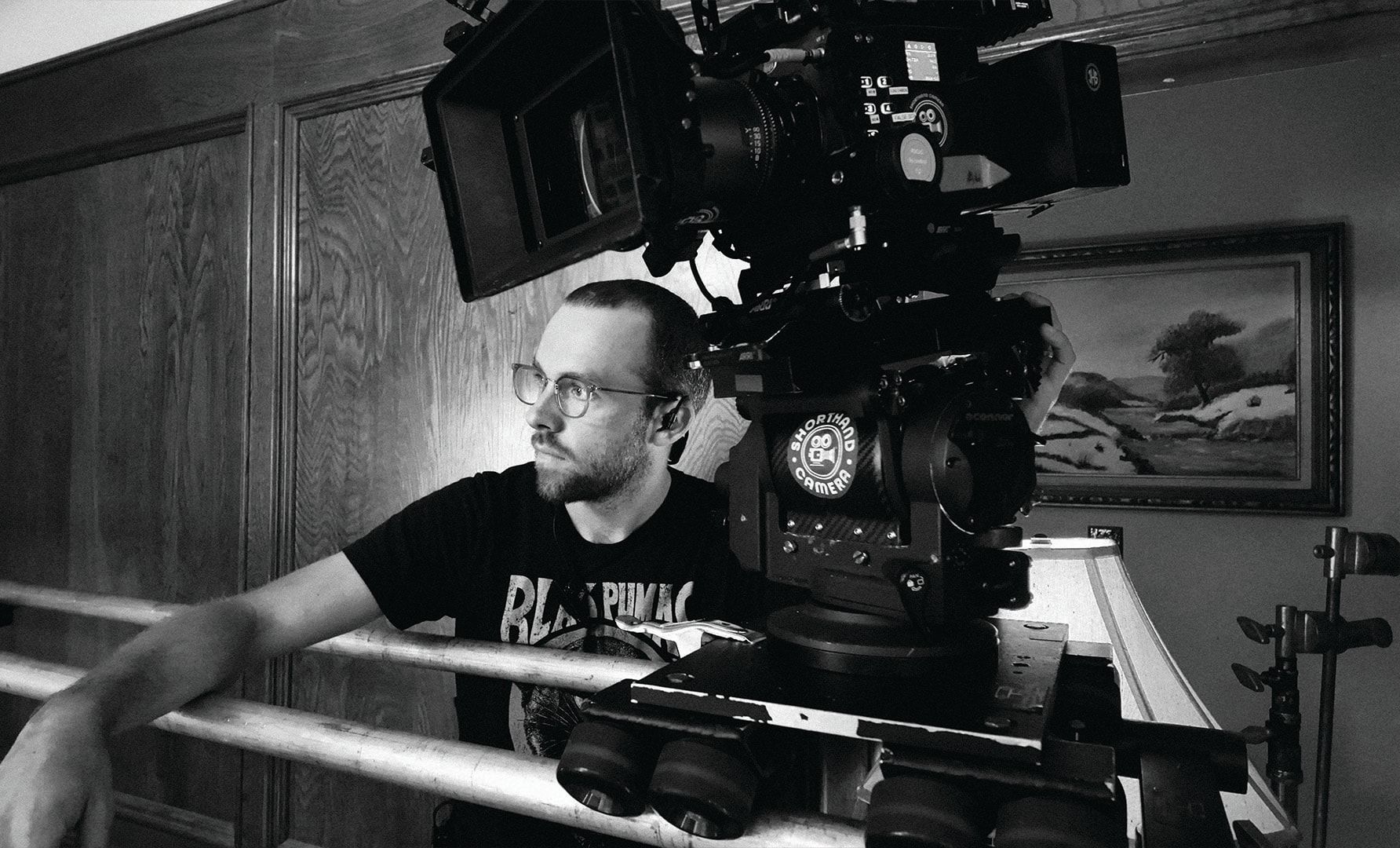The camera operator behind the camera in the wood-paneled living room, in black and white